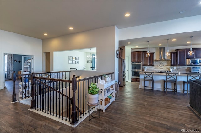 interior space with pendant lighting, a kitchen breakfast bar, stainless steel appliances, dark wood-type flooring, and wall chimney range hood