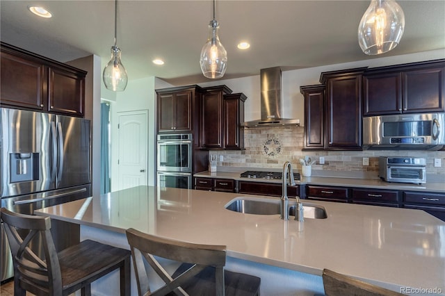 kitchen with wall chimney range hood, sink, an island with sink, and appliances with stainless steel finishes