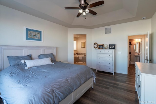 bedroom with ensuite bathroom, dark hardwood / wood-style floors, ceiling fan, and a tray ceiling