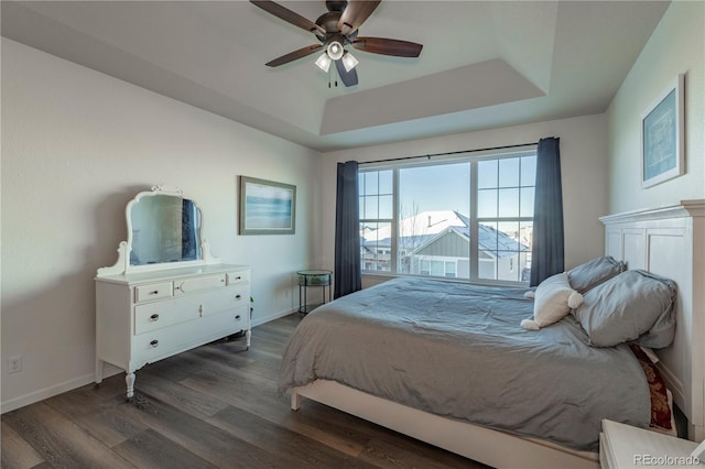 bedroom with dark hardwood / wood-style flooring, a tray ceiling, and ceiling fan