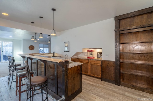 bar with hanging light fixtures, sink, and light wood-type flooring