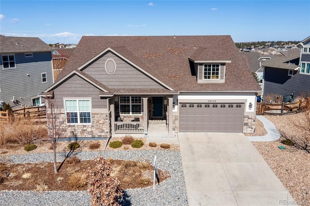 view of front of home featuring covered porch, a garage, a residential view, stone siding, and driveway