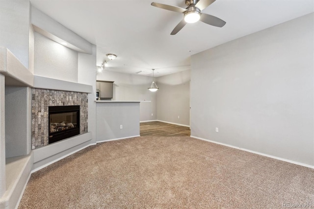 unfurnished living room featuring carpet, baseboards, ceiling fan, and a glass covered fireplace