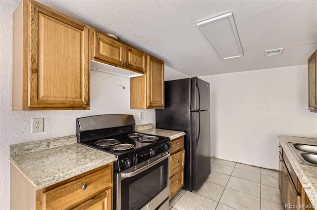 kitchen featuring light tile patterned floors, sink, black fridge, and stainless steel range with gas stovetop