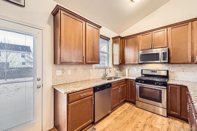 kitchen with lofted ceiling, stainless steel appliances, a sink, backsplash, and light stone countertops