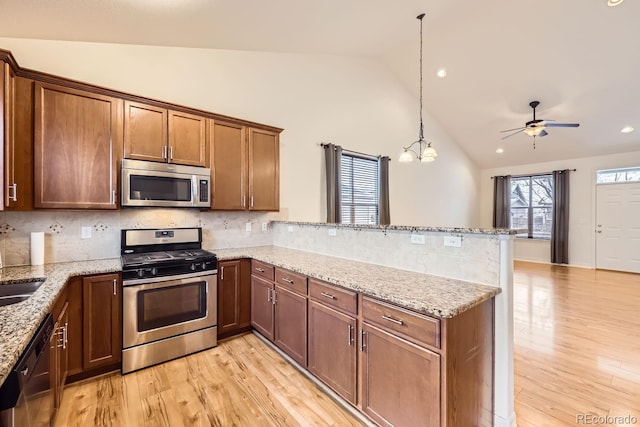 kitchen with a peninsula, appliances with stainless steel finishes, brown cabinetry, and hanging light fixtures