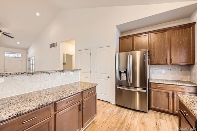 kitchen featuring brown cabinets, light stone countertops, stainless steel refrigerator with ice dispenser, and light wood finished floors