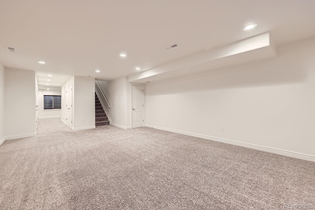 finished below grade area featuring baseboards, visible vents, light colored carpet, stairs, and recessed lighting