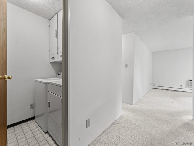 clothes washing area featuring a textured ceiling, a baseboard heating unit, washer and clothes dryer, cabinets, and light carpet