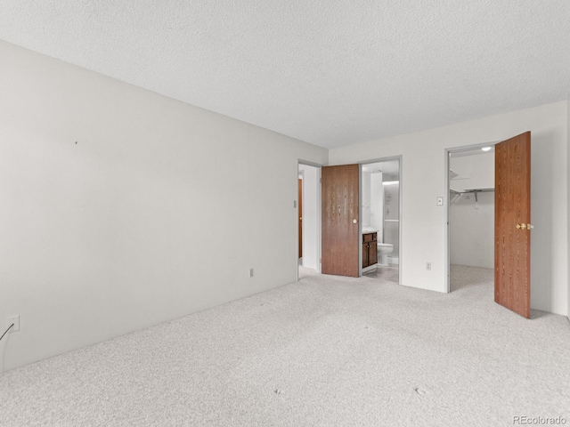 unfurnished bedroom with a spacious closet, a closet, a textured ceiling, and light carpet