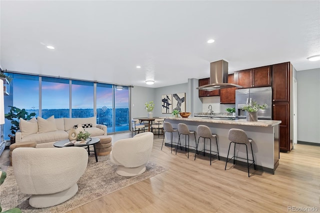 kitchen with a breakfast bar area, open floor plan, range hood, light wood finished floors, and stainless steel fridge