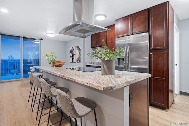 kitchen with light wood finished floors, a kitchen island, black electric cooktop, and island range hood