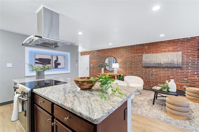 kitchen with electric stove, light wood-type flooring, brick wall, and island range hood