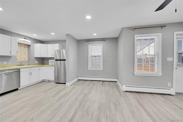 kitchen with stainless steel appliances, white cabinets, baseboard heating, and light hardwood / wood-style flooring