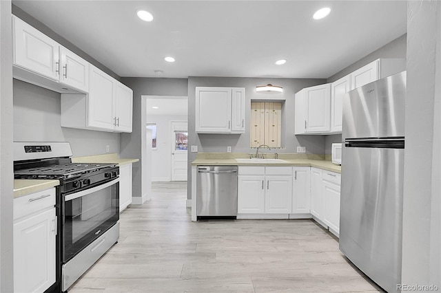 kitchen with sink, stainless steel appliances, white cabinets, and light wood-type flooring