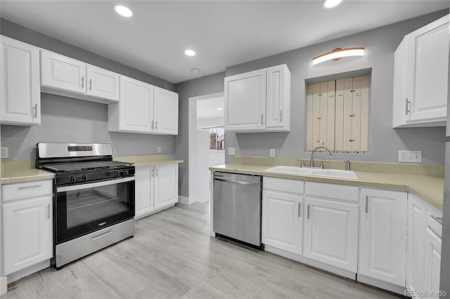 kitchen with light wood-type flooring, appliances with stainless steel finishes, sink, and white cabinets