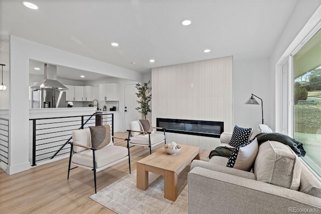 living area with recessed lighting, light wood-style floors, and a large fireplace