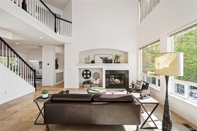 living room featuring a healthy amount of sunlight, a tile fireplace, built in features, and a towering ceiling