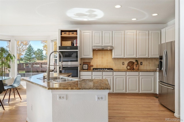 kitchen with a sink, light wood-style flooring, backsplash, white cabinetry, and appliances with stainless steel finishes