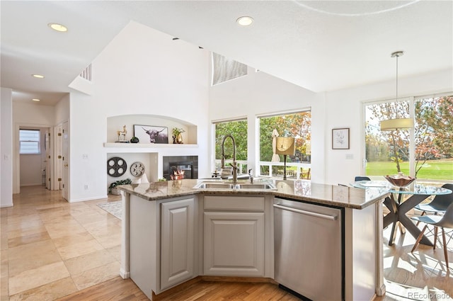 kitchen featuring a sink, a kitchen island with sink, dishwasher, light stone countertops, and a tiled fireplace