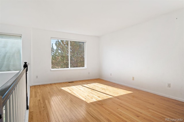 empty room with light wood finished floors, visible vents, and baseboards