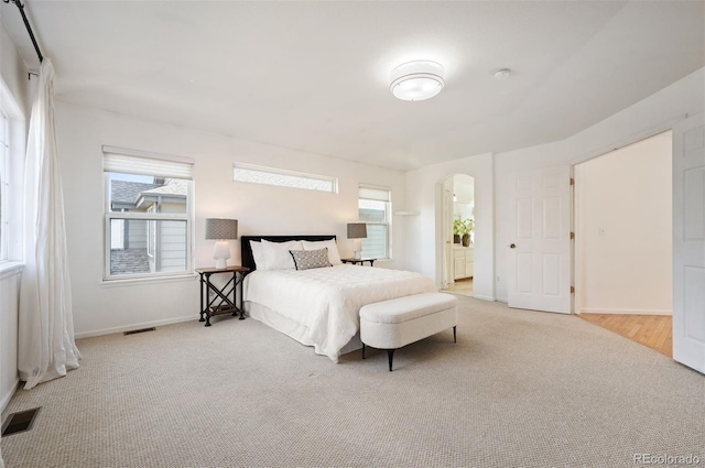 carpeted bedroom with arched walkways, ensuite bathroom, baseboards, and visible vents