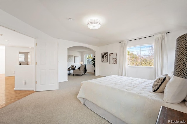 carpeted bedroom featuring baseboards and arched walkways