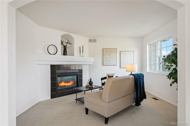 carpeted living area with baseboards, a tile fireplace, and visible vents