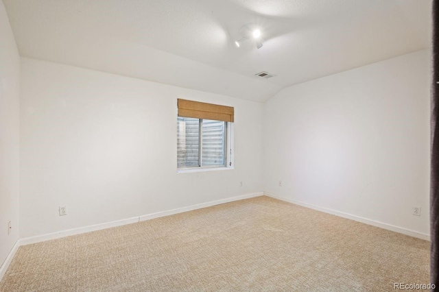 spare room with light carpet, baseboards, lofted ceiling, and visible vents