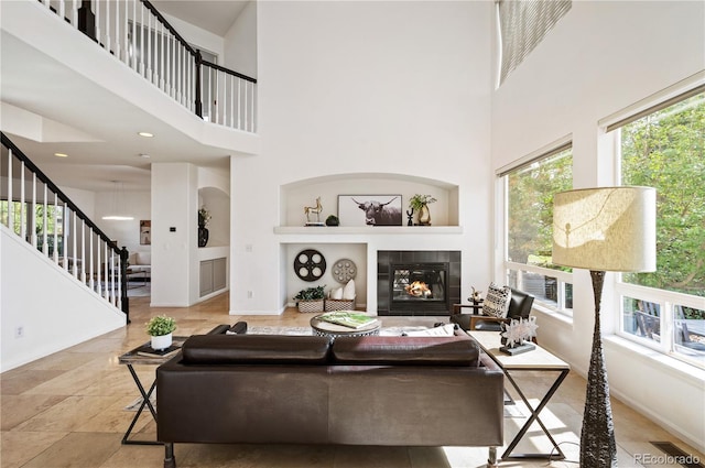 living area featuring baseboards, stairway, a fireplace, and a high ceiling