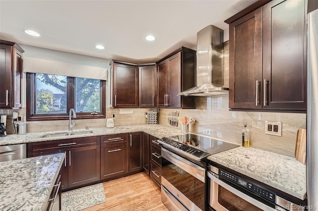 kitchen featuring appliances with stainless steel finishes, wall chimney range hood, sink, light stone counters, and light hardwood / wood-style flooring