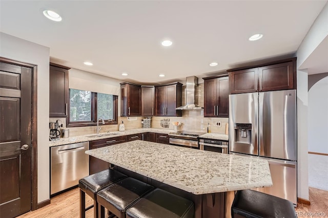 kitchen with a breakfast bar, wall chimney exhaust hood, stainless steel appliances, and a kitchen island