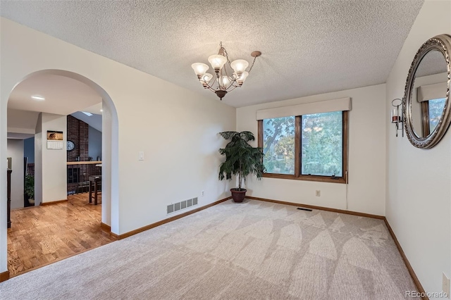 unfurnished room featuring light carpet, an inviting chandelier, and a textured ceiling