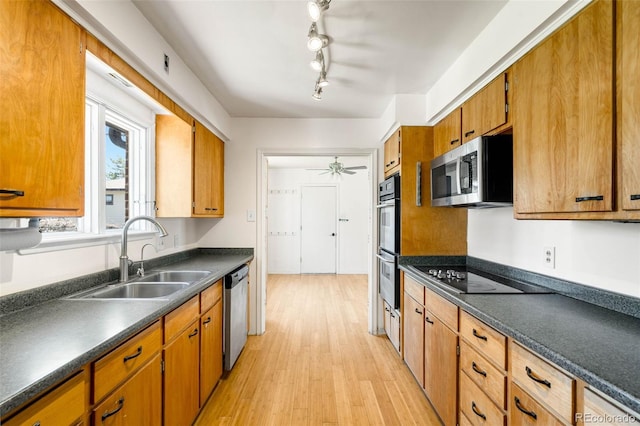 kitchen with a sink, appliances with stainless steel finishes, dark countertops, light wood-style floors, and brown cabinets
