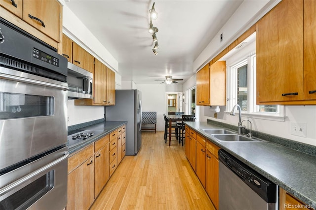 kitchen with appliances with stainless steel finishes, a sink, dark countertops, light wood-style flooring, and a ceiling fan