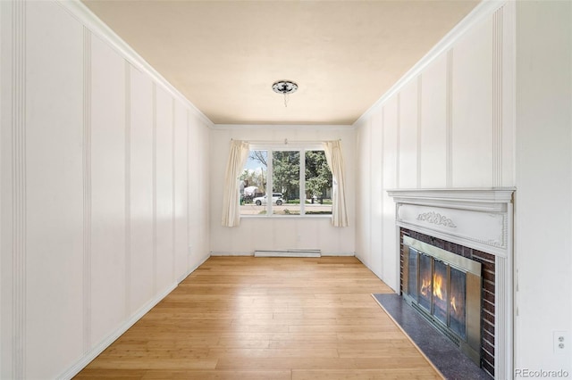unfurnished living room with a baseboard heating unit, a fireplace with flush hearth, light wood-style flooring, a decorative wall, and crown molding