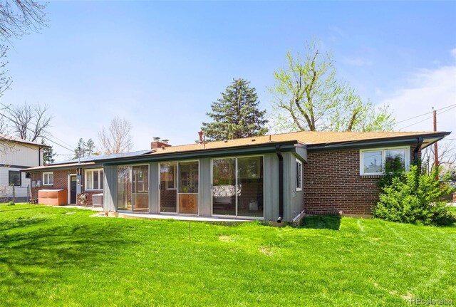 rear view of house featuring a chimney, a lawn, and brick siding