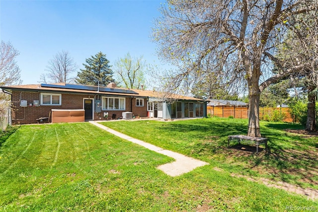 rear view of property with a sunroom, brick siding, solar panels, central air condition unit, and a chimney