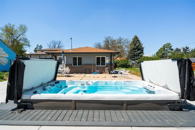 rear view of property with a covered hot tub, brick siding, and a wooden deck