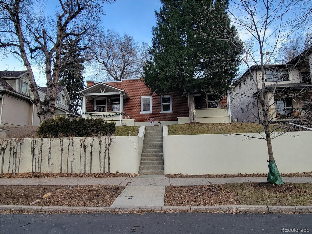 bungalow featuring covered porch, brick siding, a chimney, and stairs