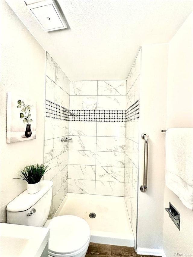 bathroom with hardwood / wood-style floors, toilet, and a tile shower