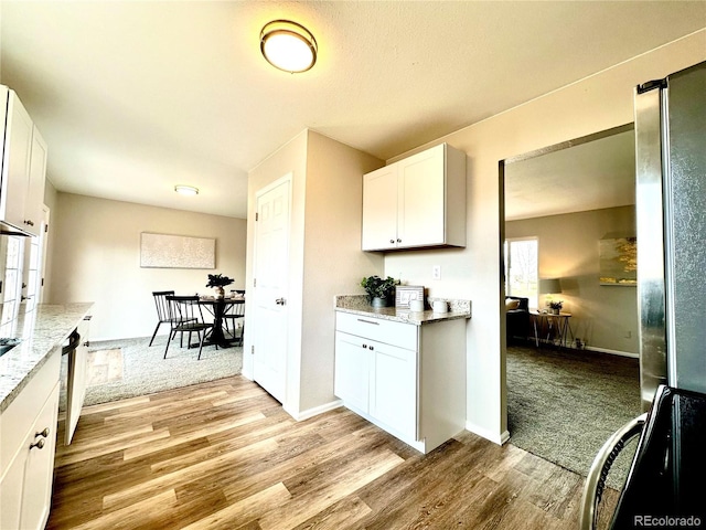 kitchen featuring light stone countertops, light wood-type flooring, white cabinetry, and stove