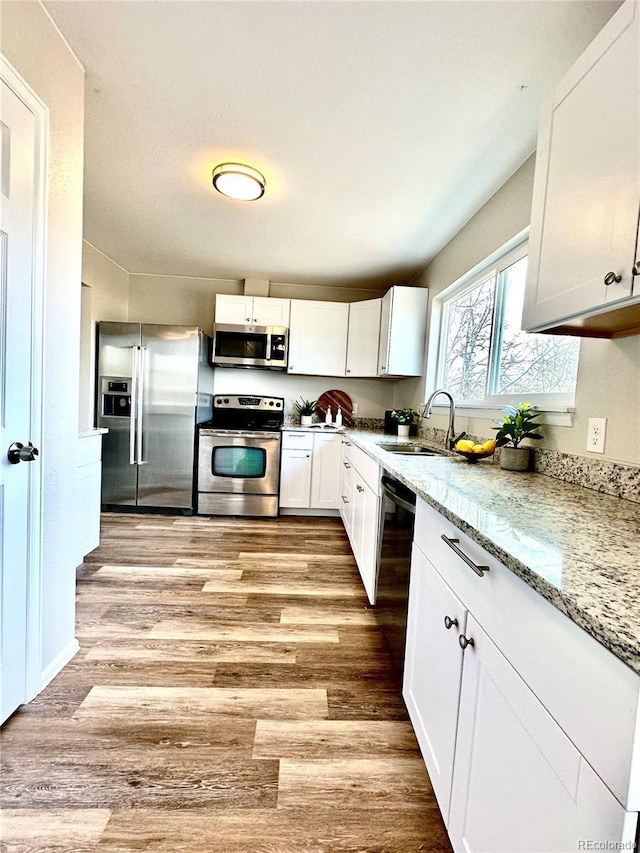 kitchen with light stone countertops, white cabinetry, sink, appliances with stainless steel finishes, and light wood-type flooring