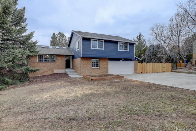 tri-level home with concrete driveway, brick siding, an attached garage, and fence