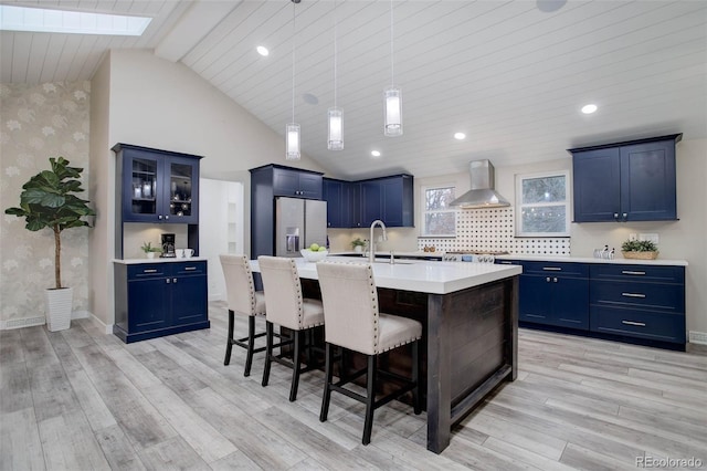 kitchen featuring wall chimney exhaust hood, a kitchen breakfast bar, blue cabinets, stainless steel fridge with ice dispenser, and wallpapered walls