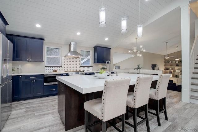 kitchen featuring blue cabinets, a kitchen breakfast bar, light countertops, wall chimney range hood, and stainless steel fridge