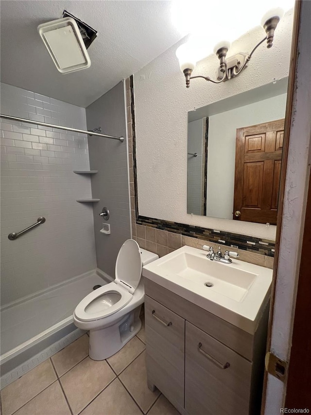 bathroom with toilet, tile patterned flooring, vanity, a tile shower, and backsplash