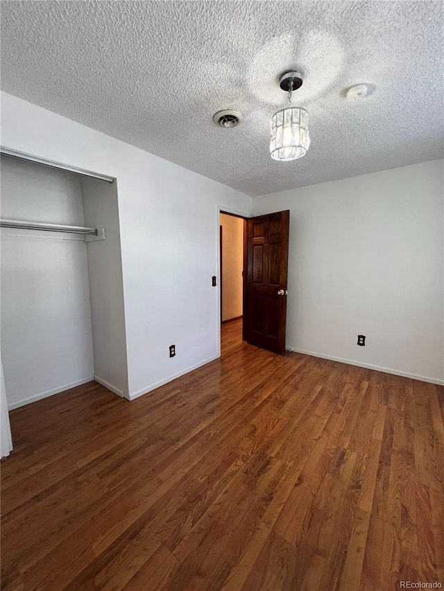 unfurnished bedroom with a textured ceiling, dark hardwood / wood-style flooring, a notable chandelier, and a closet