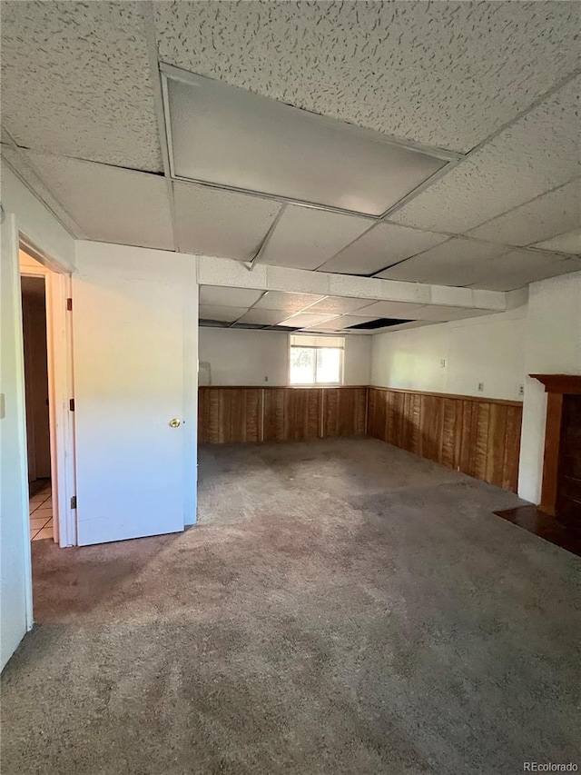 interior space with a paneled ceiling, wood walls, and carpet floors