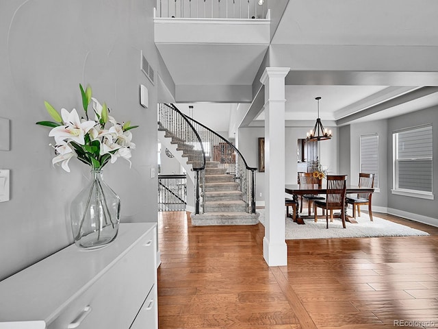 foyer entrance featuring ornate columns, hardwood / wood-style flooring, a notable chandelier, and a tray ceiling